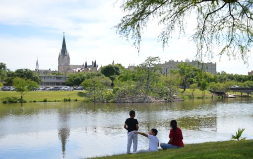Family sitting on the banks of Elmendorf Lake with Our Lady of the Lake University in the background.