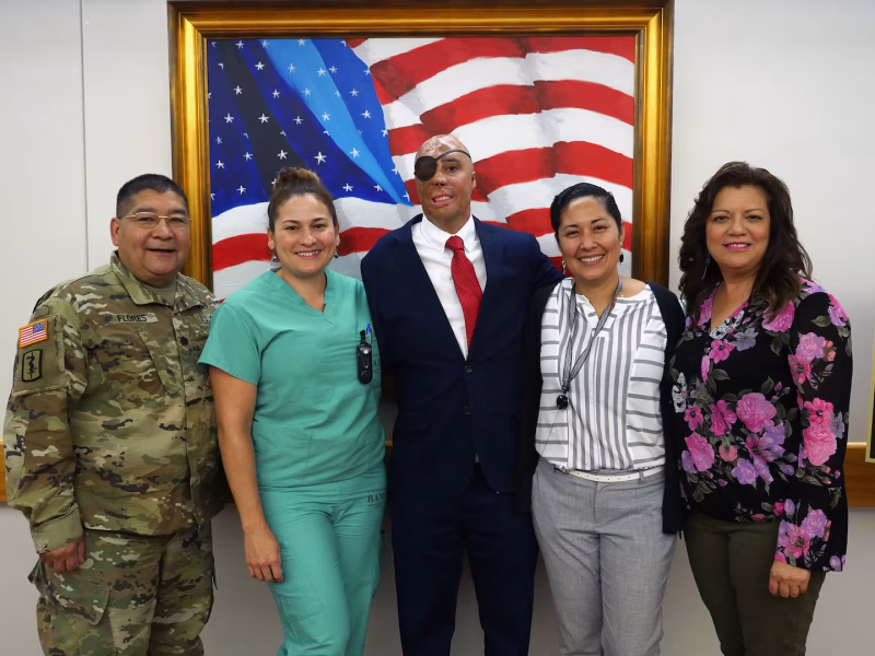 Sgt. Mario Lopez, center, in front of his painting of the American Flag that hangs at Brooke Army Medial Center (BAMC).